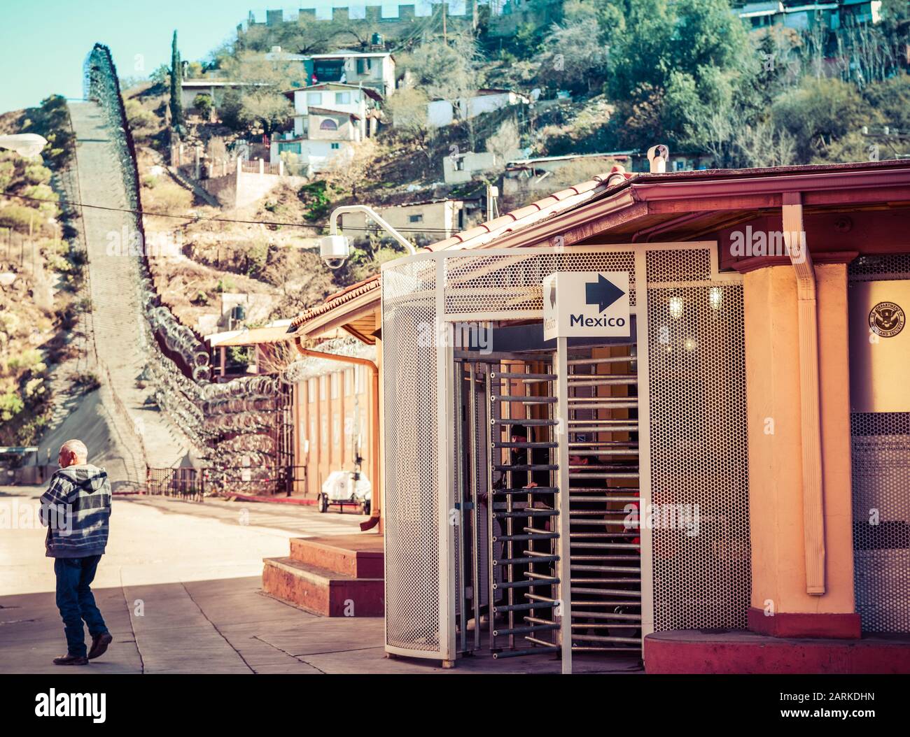 Persone che attraversano il confine USA/Messico a piedi al Punto Di Ingresso Al Confine con la porta Morley negli Stati Uniti con recinzione di confine e case messicane sullo sfondo Foto Stock