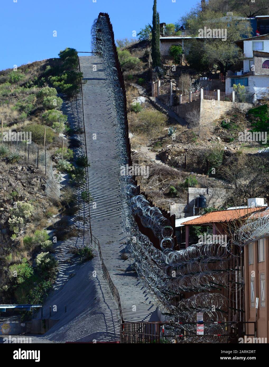 Vista della recinzione di confine internazionale di metallo USA/Messico con filo di rasoio in salita con le case messicane sull'altro lato della recinzione da Nogales, AZ, USA Foto Stock