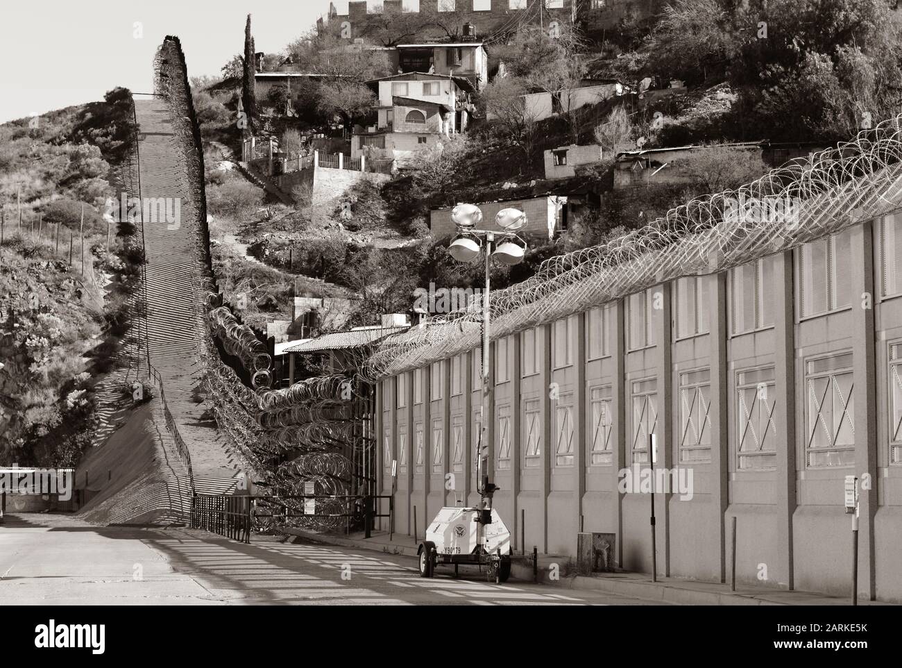 Vista del confine internazionale USA/Messico con filo di rasoio in salita con le case messicane sull'altro lato del recinto da Nogales, AZ, USA, seppia Foto Stock