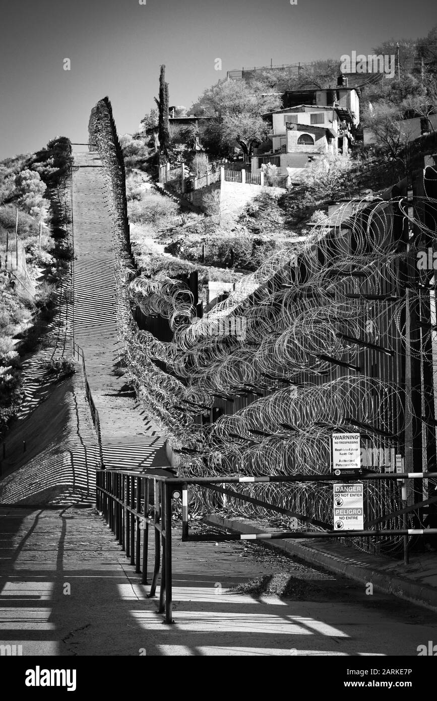 Vista della recinzione di confine internazionale USA/Messico con filo di rasoio in salita con le case messicane sull'altro lato della recinzione da Nogales, AZ, USA, in bl Foto Stock