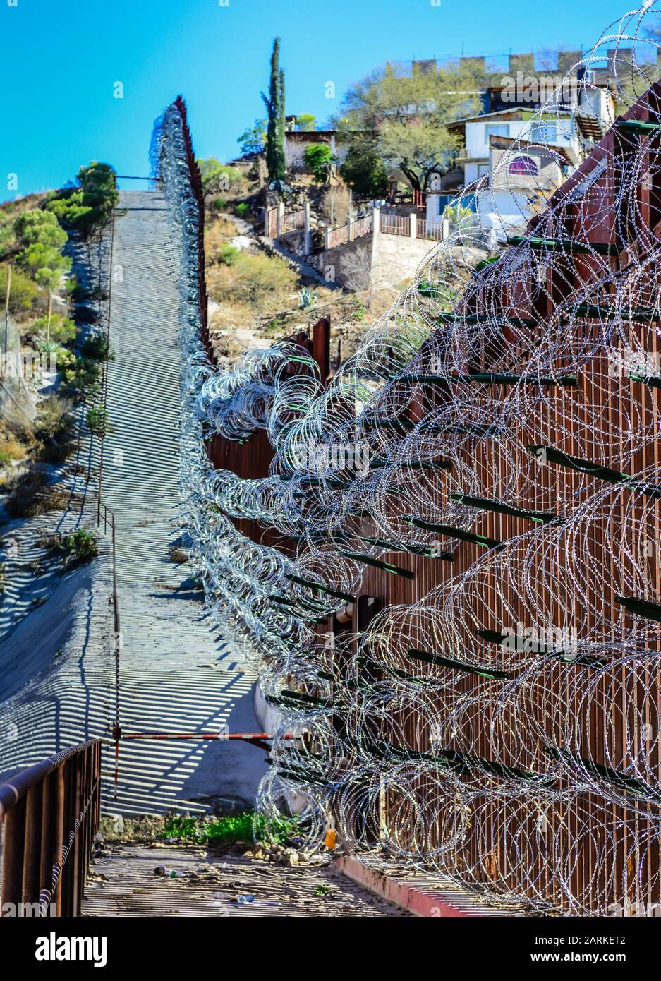 Vista della recinzione di confine internazionale di metallo USA/Messico con filo di rasoio che segue la salita tra Nogales, AZ, USA e Nogales, sonora, MX, Foto Stock