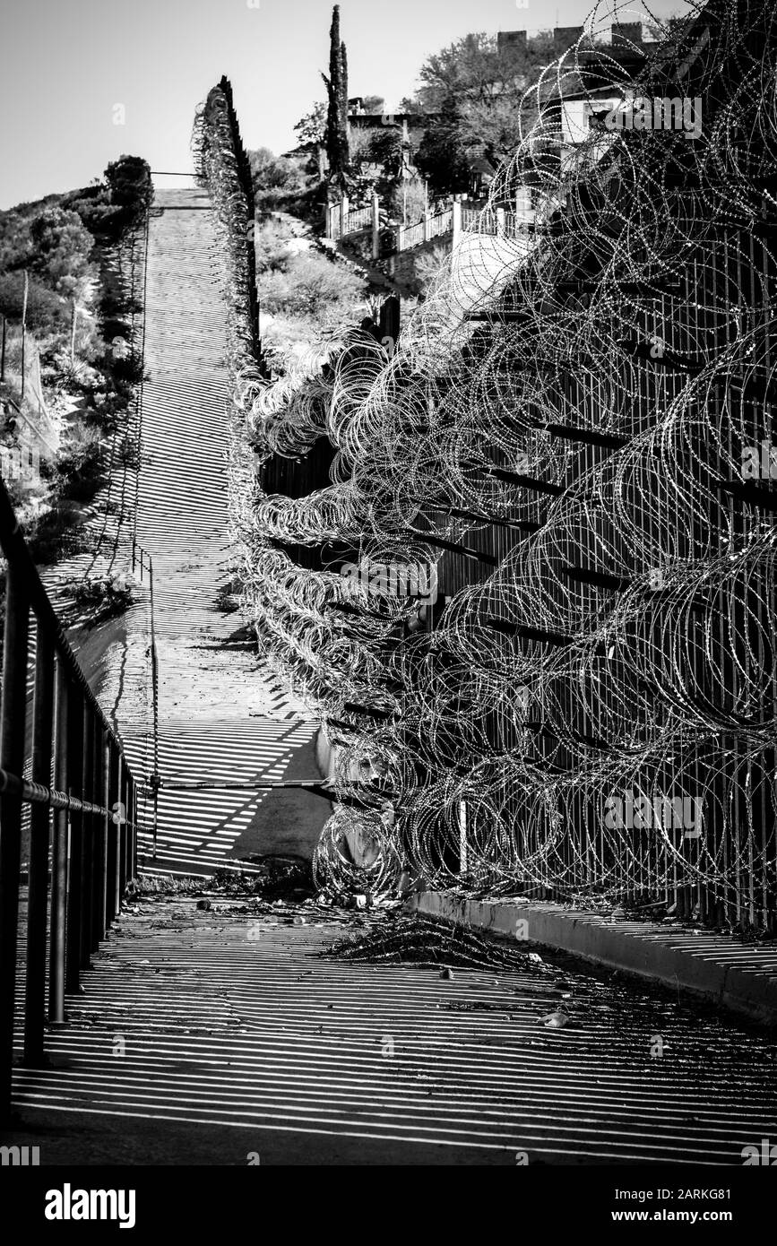 Vista della recinzione di confine internazionale USA/Messico con filo di rasoio in salita con le case messicane sull'altro lato della recinzione da Nogales, AZ, USA, in bl Foto Stock