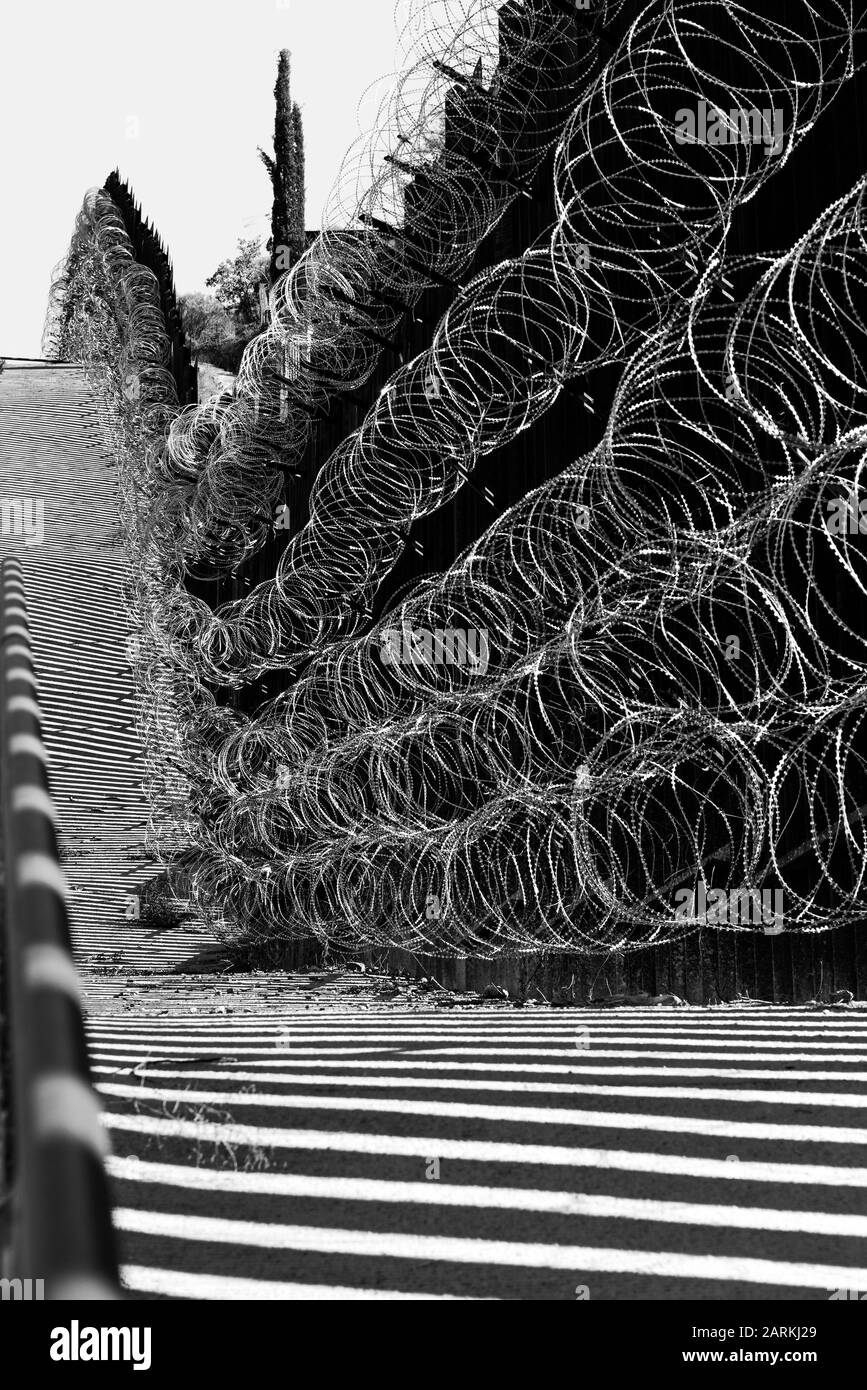 Vista del confine internazionale USA/Messico con filo di rasoio in salita con il Messico dall'altro lato del recinto da Nogales, AZ, USA, in B&W. Foto Stock