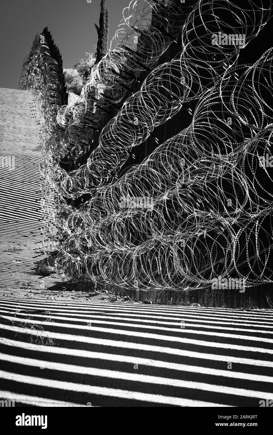 Vista del confine internazionale USA/Messico con filo di rasoio in salita con il Messico dall'altro lato del recinto da Nogales, AZ, USA, in B&W. Foto Stock