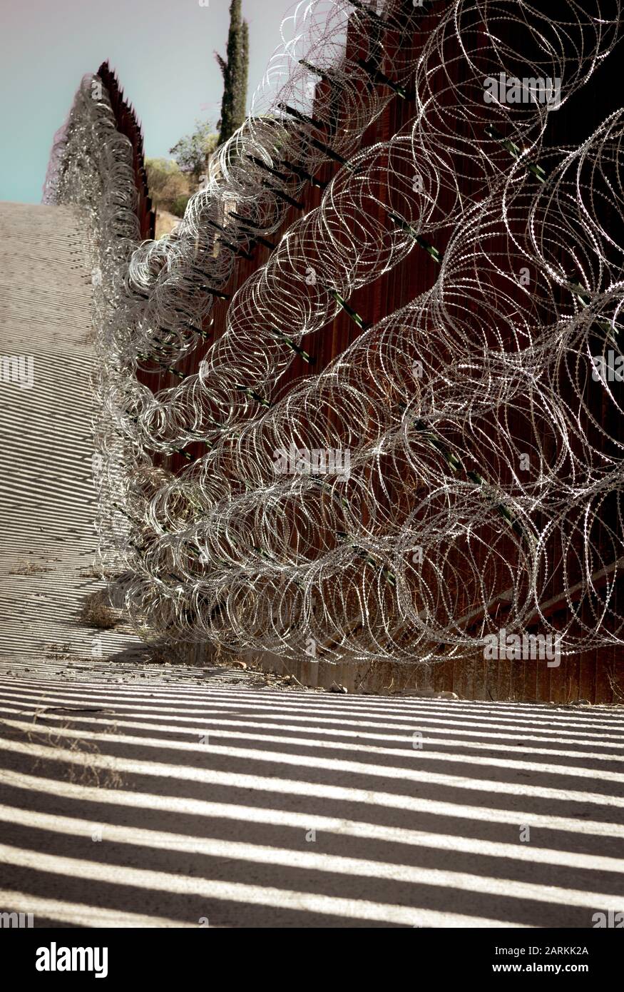 Vista della recinzione di confine internazionale di metallo USA/Messico con filo di rasoio che segue la salita tra Nogales, AZ, USA e Nogales, sonora, MX, Foto Stock