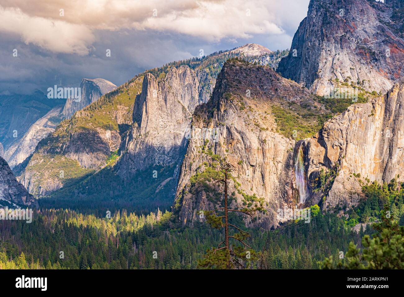 Arcobaleno sopra la Caduta di Bridalveil nel parco nazionale di Yosemite, California. Presenta inoltre Cathedral Rocks, Half Dome e Cloud Rest coperti da nuvole. Foto Stock