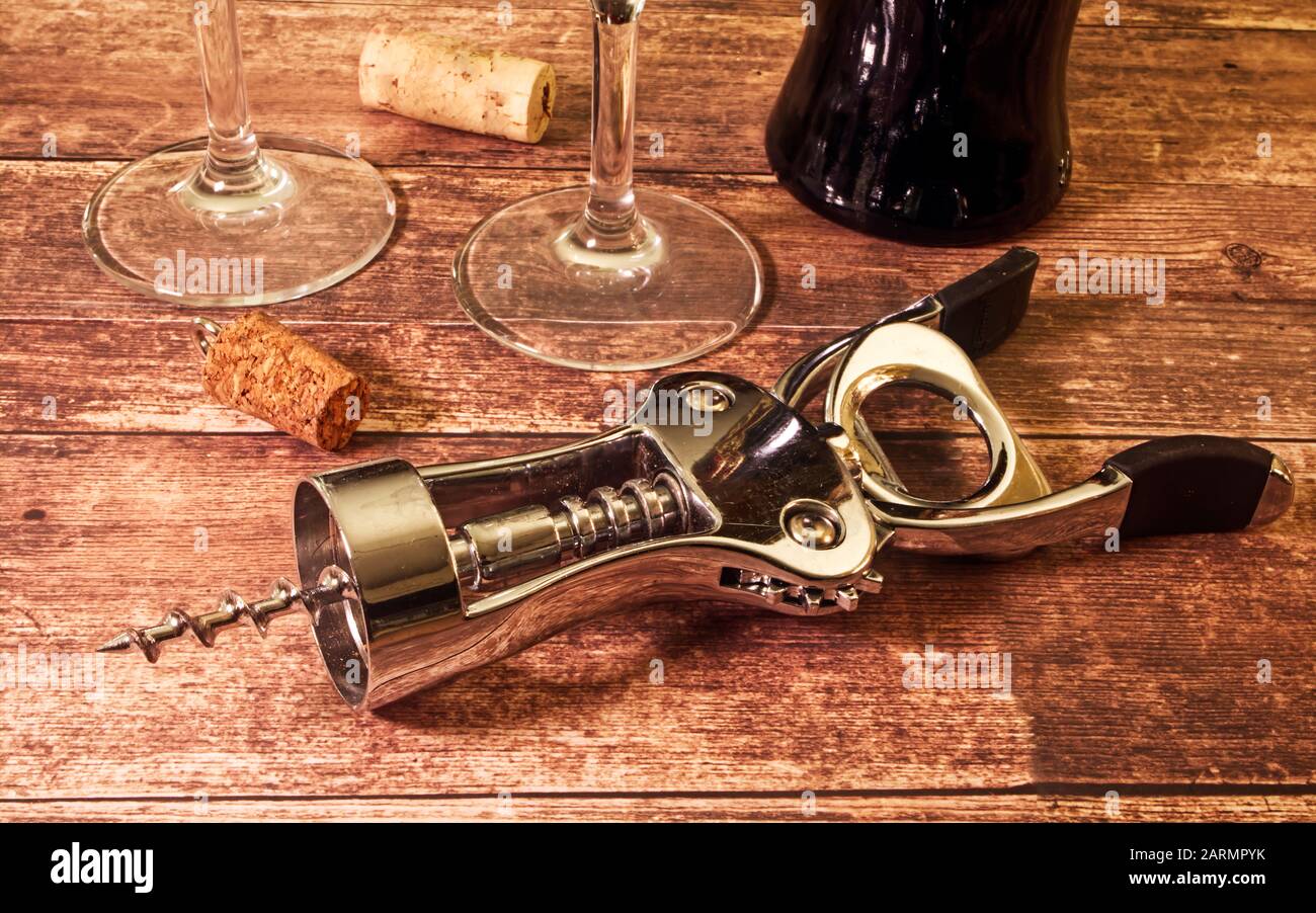 Cavatappi in metallo su fondo in legno. Bottiglia di vino rosso, bicchieri e tappi Foto Stock