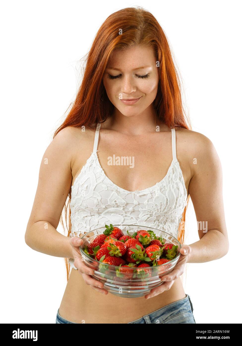 Foto di una bellissima giovane donna con lunghi capelli rossi tenendo una tazza di fragole su sfondo bianco. Foto Stock