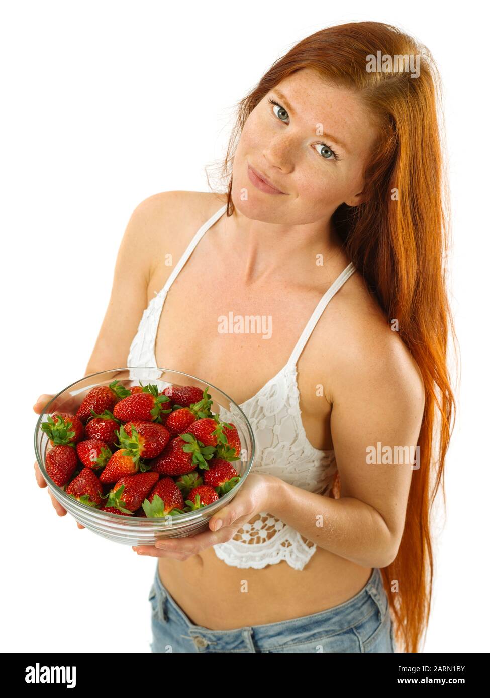 Foto di una bellissima giovane donna con lunghi capelli rossi tenendo una tazza di fragole su sfondo bianco. Foto Stock