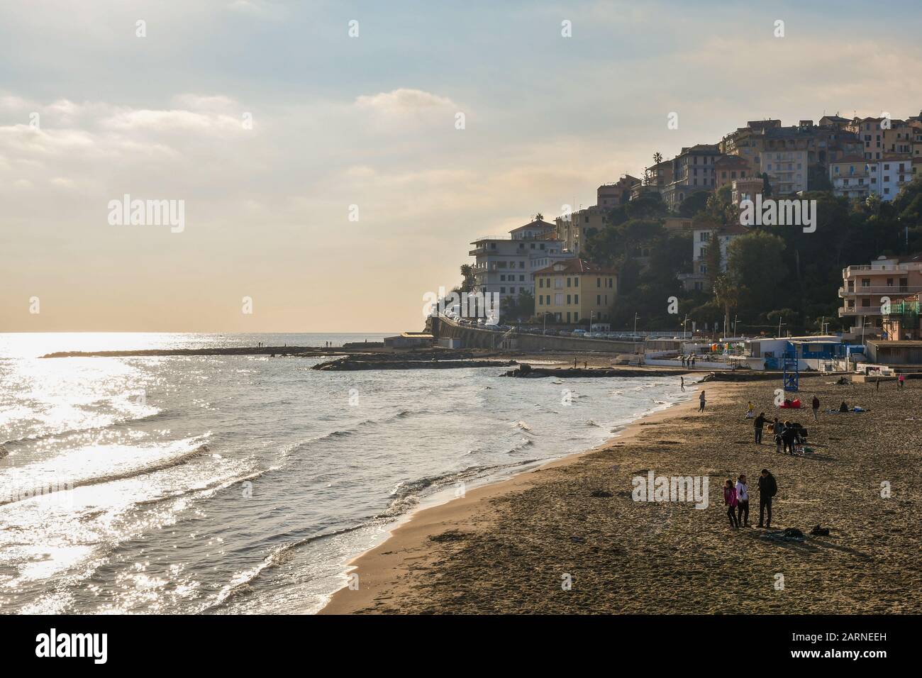 Spiaggia di sabbia di Porto Maurizio con persone che si godono il sole in una calda giornata invernale e il borgo antico di Parasio sul capo, Imperia, Liguria, Italia Foto Stock