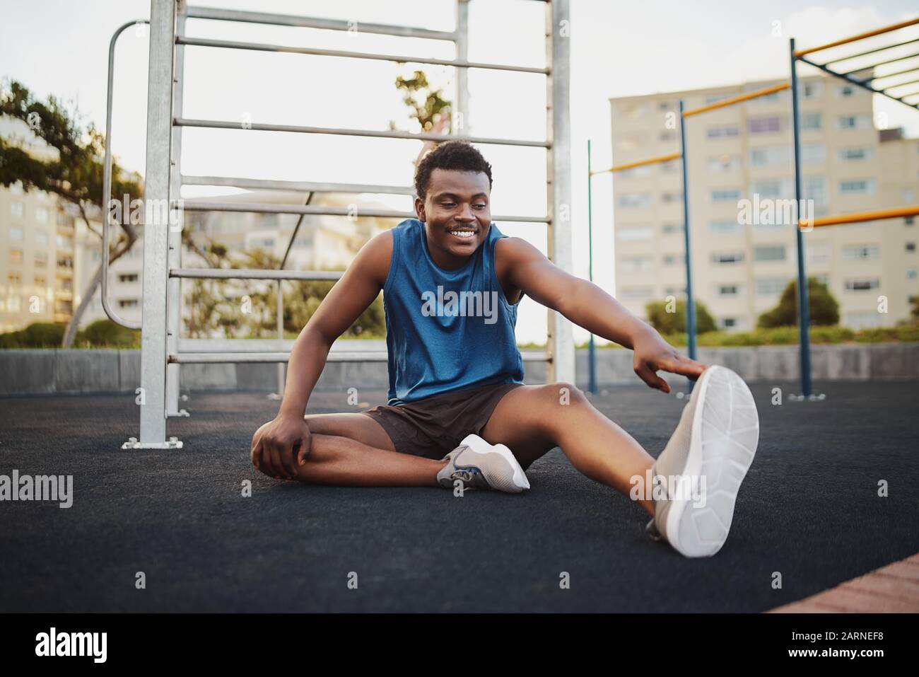 Ritratto di un uomo sorridente runner seduto su palestra all'aperto parco gambe stretching preparazione per la corsa di allenamento Foto Stock