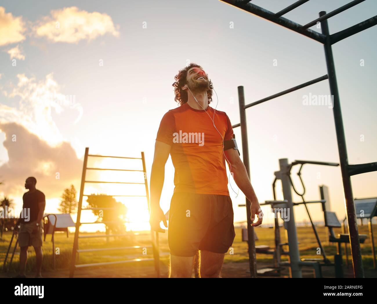 Felice uomo giovane che si gode ascoltare la musica sulle cuffie dopo l'esercizio nel parco all'aperto palestra in estate giornata di sole Foto Stock