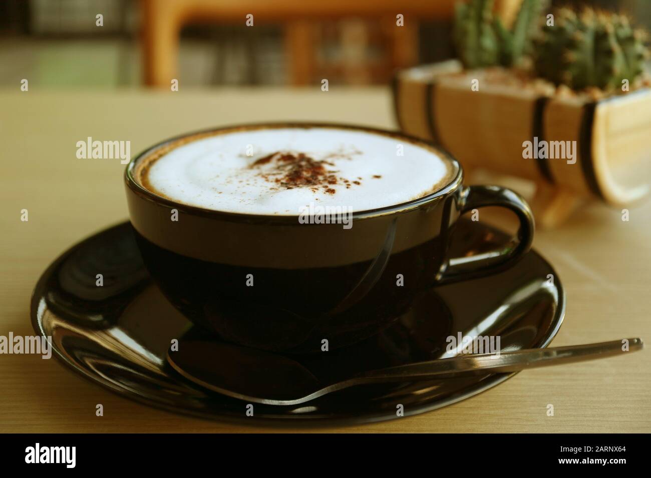 Cappuccino caffè in una tazza nera servito su tavolo di legno Foto Stock