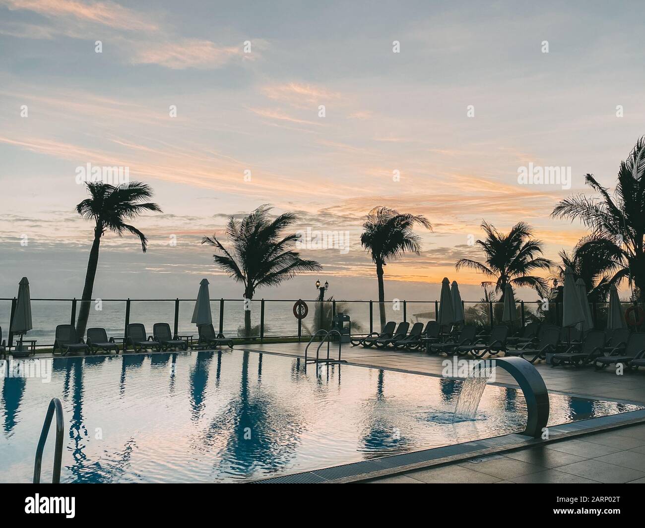 Piscina, palme intorno, riflessione di palme in piscina, alba con un bel cielo nuvoloso. Un'area vuota con molti lettini, il pas del sole Foto Stock