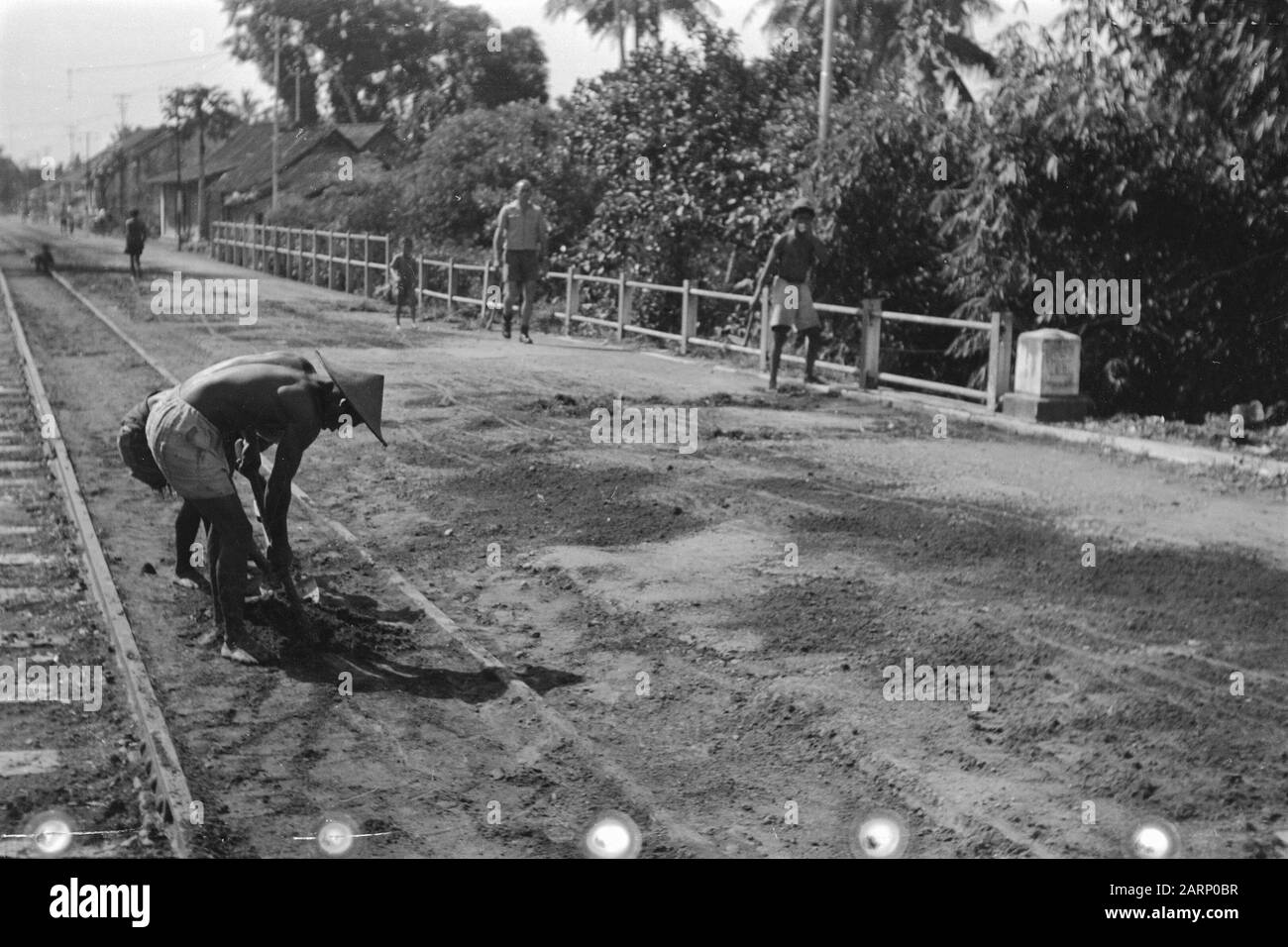 Moentilan tra Djokja e Magelang Due uomini indonesiani scavano una fossa in una strada con ponte e binari ferroviari o tram Data: 1 febbraio 1949 luogo: Indonesia, Muntilan, Indie olandesi Foto Stock