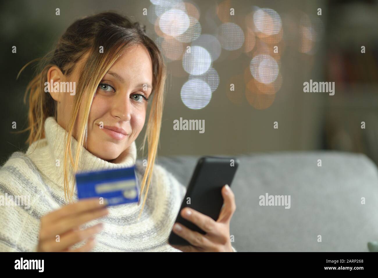La donna soddisfatta che compra in linea che osserva voi seduta su un divano a casa nella notte in inverno Foto Stock