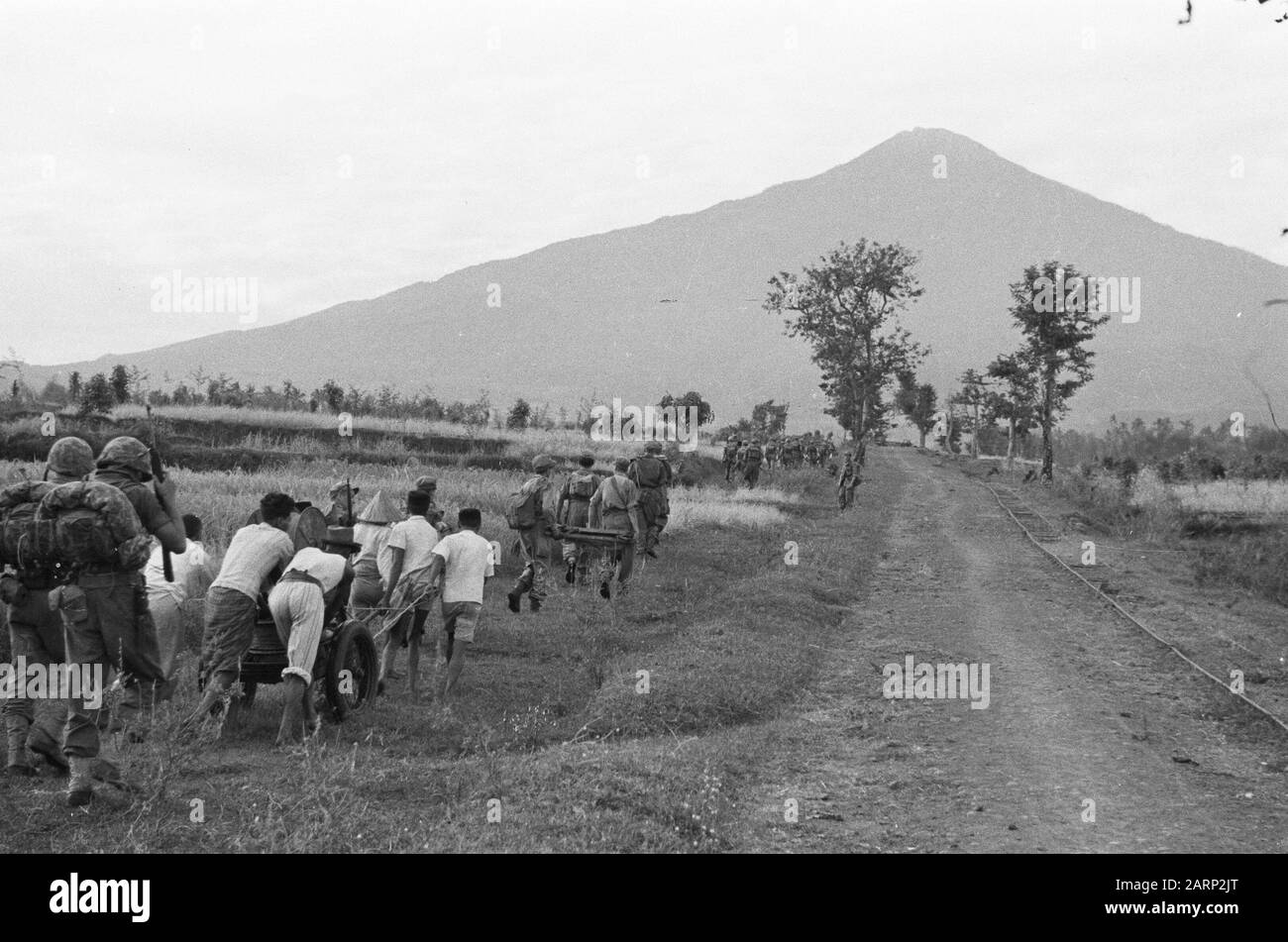 Avanzamenti di Poegeran a Patjet 3-5 Reggimento Fanteria settore Surabja. In molti luoghi le truppe olandesi sono state accolte con entusiasmo dalla popolazione mentre marciò. In anticipo da Poegeran a Patjet, molti indonesiani offrirono il loro aiuto, che fu accettato dai nostri uomini. Annotazione: Gli aiutanti indonesiani tirano una funivia. Ci sembrano essere marines con un pacchetto. Sullo sfondo un vulcano (Gunung Arjuna o Arjuno?) Data: 23 luglio 1947 luogo: Indonesia, Java, Indie Orientali Olandesi Foto Stock