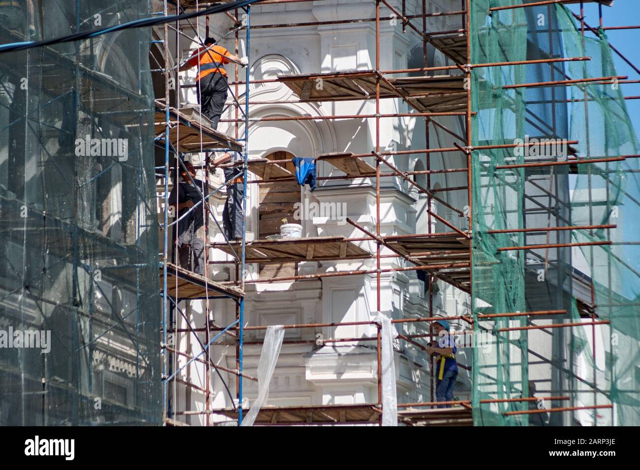 Lavoratori in uniformi di colore su ponteggi che riparano la facciata di un edificio leggero Foto Stock