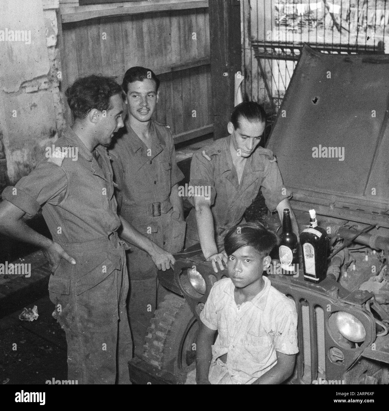 [Ragazzo indonesiano siede di fronte a una jeep e guarda nelle lesne. Ha tre soldati con lui. Dietro di lui sul radiatore di una jeep con motore aperto coprire due bottiglie. Una delle bottiglie ha un coagulo nel collo (molotov cocktail?)] Annotation: DJK Date: 1947/01/01 Location: Indonesia, Dutch East Indies Foto Stock