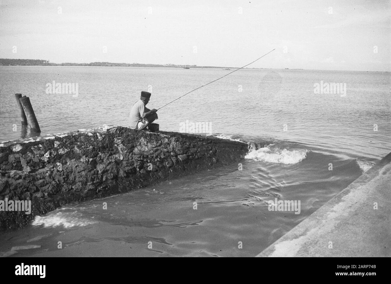 Pescatore seduto su breakwater Data: 1947/01/01 luogo: Indonesia, Indie orientali olandesi Foto Stock