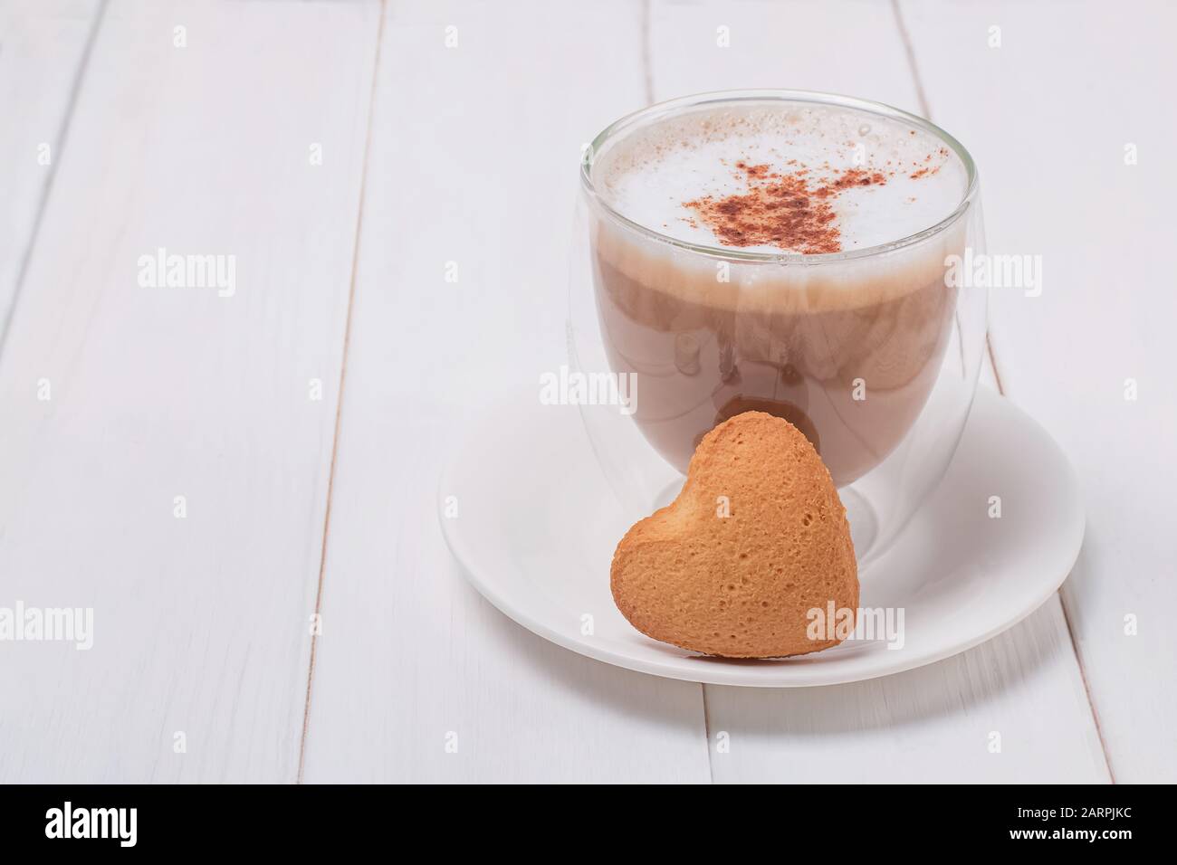 Una tazza di caffè e un biscotto a forma di cuore dolce sul tavolo bianco Foto Stock