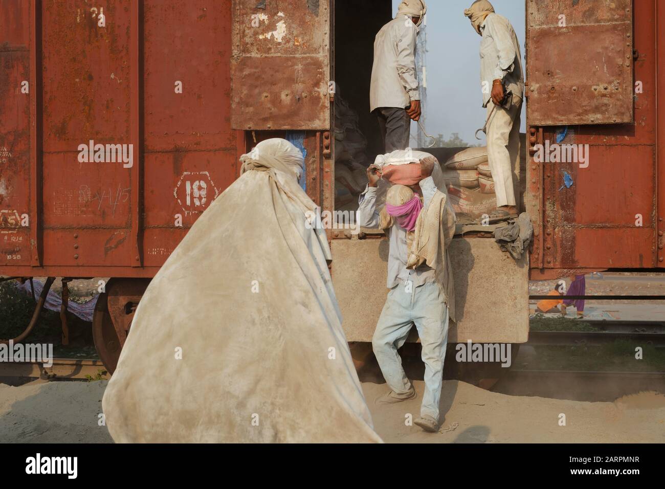 Team di lavoratori di sesso maschile in condizioni polverose spostare pesanti sacchi di cemento da treno nella calda estate condizioni in Mathura, Uttar Pradesh, India. Foto Stock