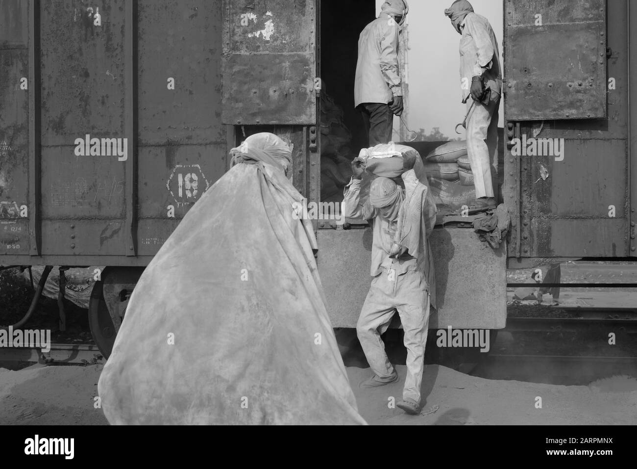 Team di lavoratori di sesso maschile in condizioni polverose spostare pesanti sacchi di cemento da treno nella calda estate condizioni in Mathura, Uttar Pradesh, India. Foto Stock