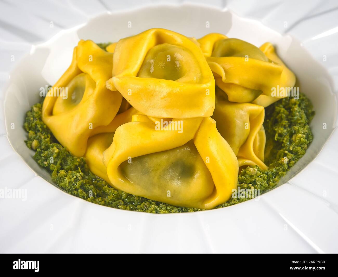 Tortelloni tradizionali italiani freschi con salsa al pesto, su un elegante piatto bianco Foto Stock