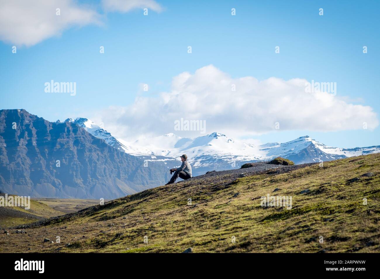 Giovane uomo guarda fuori nel terreno aspro lontano e le montagne innevate dei vividi paesaggi naturali dell'Islanda Foto Stock