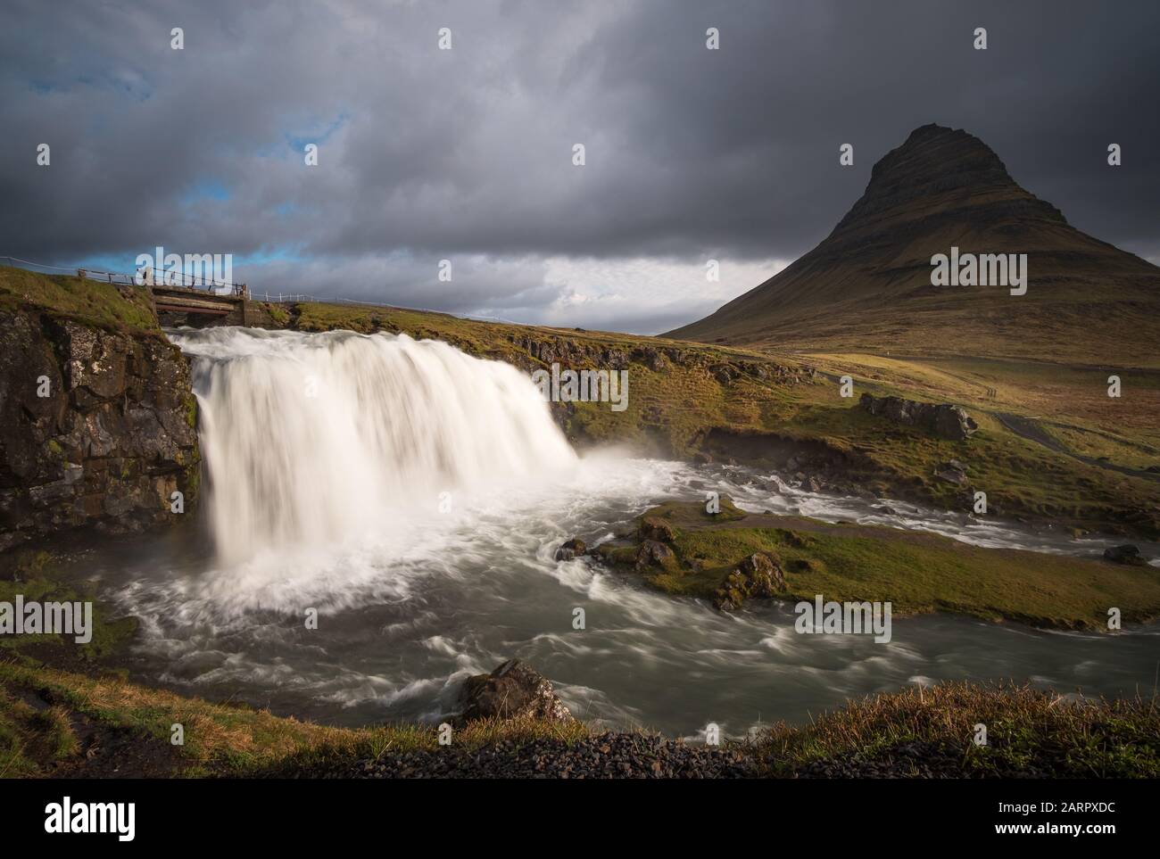 Un ponte sopra la cascata infuriante di Kirkjufellsfoss e vicino all'epica montagna Kirkjufell sulla costa settentrionale della penisola dell'Islanda Snæfellsnes Foto Stock