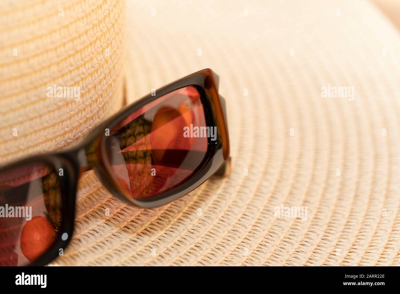 Sunglassess e cappello di paglia simboleggiano le vacanze e viaggiare nei paesi caldi. I frutti tropicali si riflettono nelle tonalità del sole. Immagine a colori con spazio di copia Foto Stock