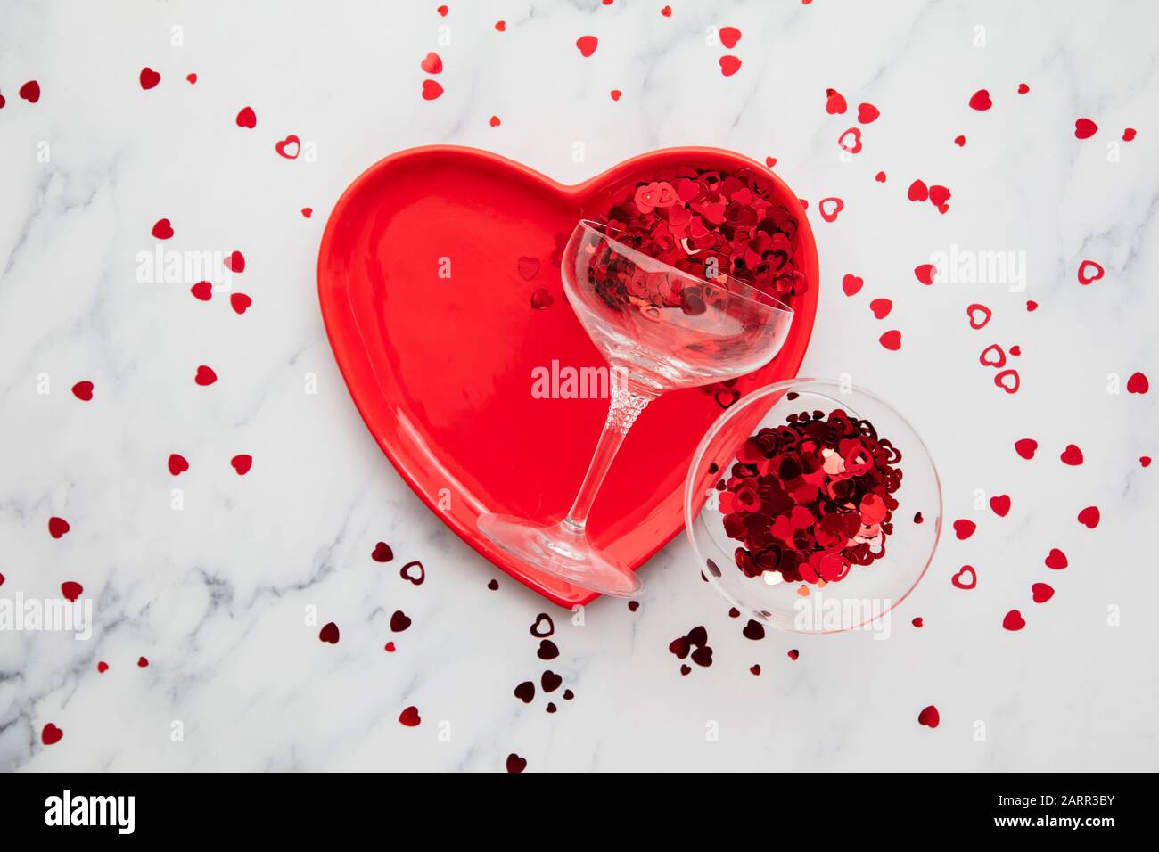 Cena di San Valentino. Piastra a cuore rossa con champagne e confetti Foto Stock