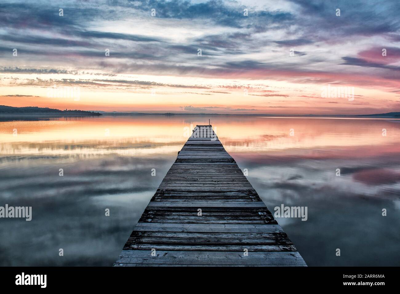 San Feliciano, Lago Trasimeno, Perugia, Umbria, Italia. Una passerella in legno guida lo sguardo sul tramonto verso il Lago Trasimeno, con un bel tramonto. Foto Stock