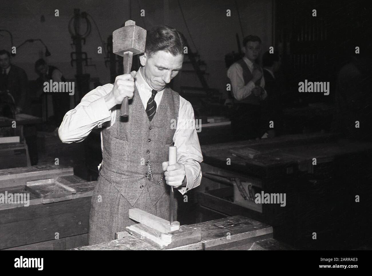 Anni '1940, storico, un gentiluomo britannico vestito in modo intelligente che indossa una camicia, una cravatta e un gilet utilizzando un martello di legno e uno scalpello in metallo in una classe educativa per adulti di lavorazione del legno, Londra, Inghilterra, Regno Unito. C'è stato un notevole aumento dell'educazione degli adulti e l'enfasi nell'apprendimento di nuove competenze nel Regno Unito post-seconda guerra mondiale. Foto Stock