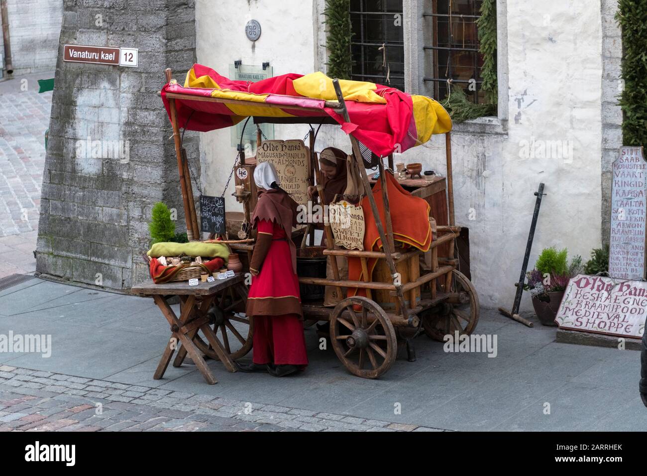 Vagone in stile medievale con donne vestite con abiti tradizionali medievali, che vendono cibo ai passanti. Tallinn, Estonia Foto Stock
