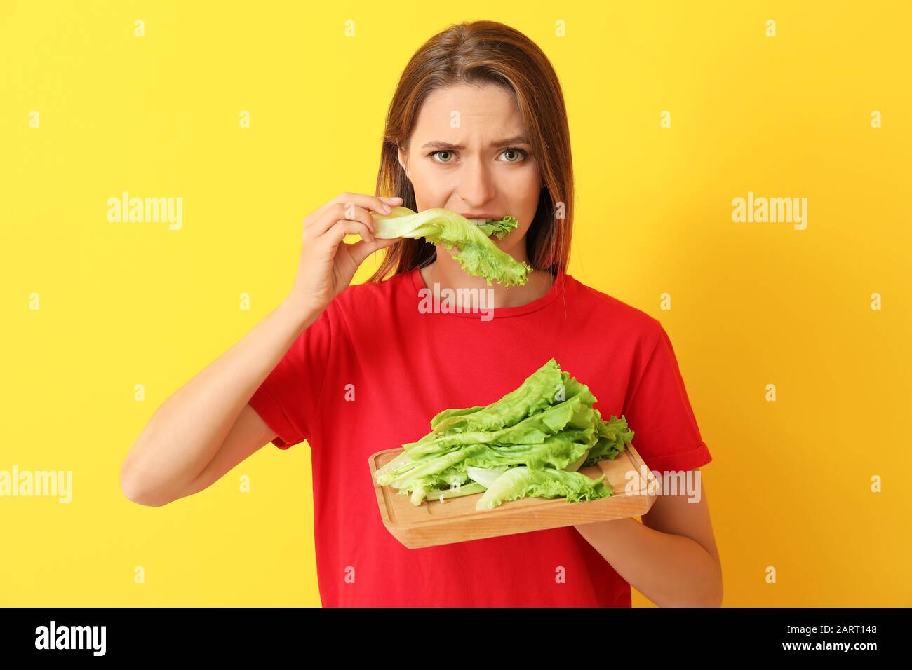 Donna stressata che mangia lattuga sana su sfondo colorato. Concetto di dieta Foto Stock