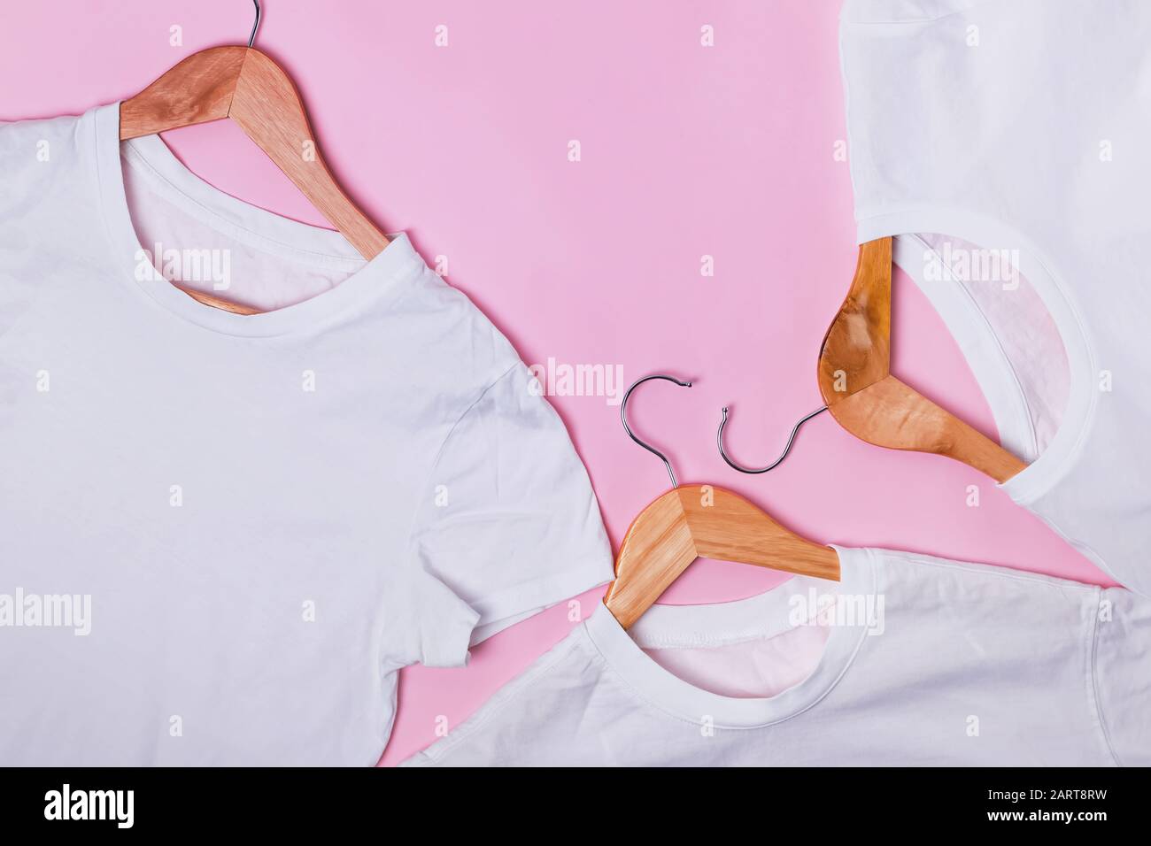 Magliette bianche su appendiabiti in legno su sfondo rosa Foto Stock