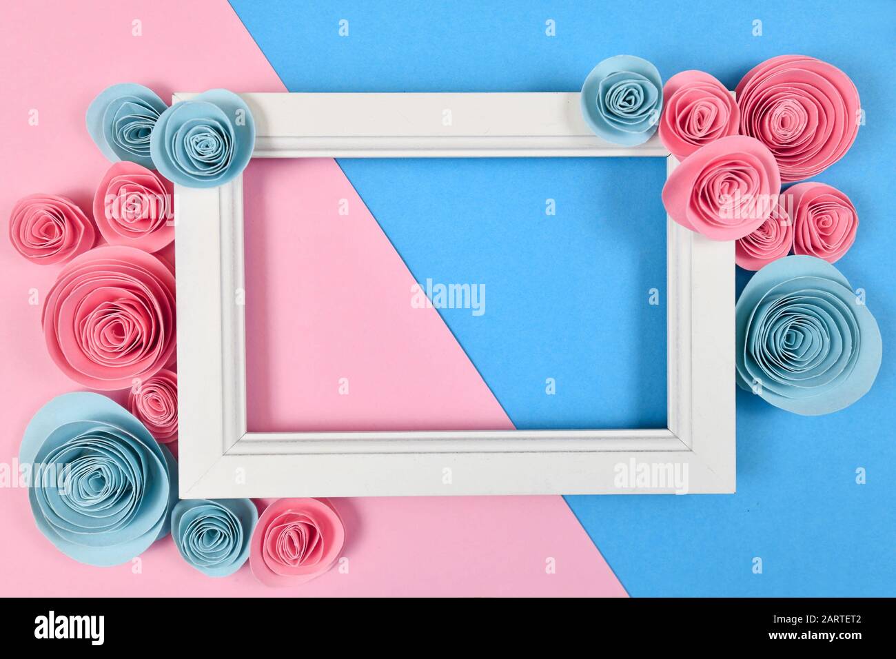 Cute piatto con cornice bianca vuota circondata da romantiche rose artigianali di carta su sfondo blu pastello e rosa Foto Stock