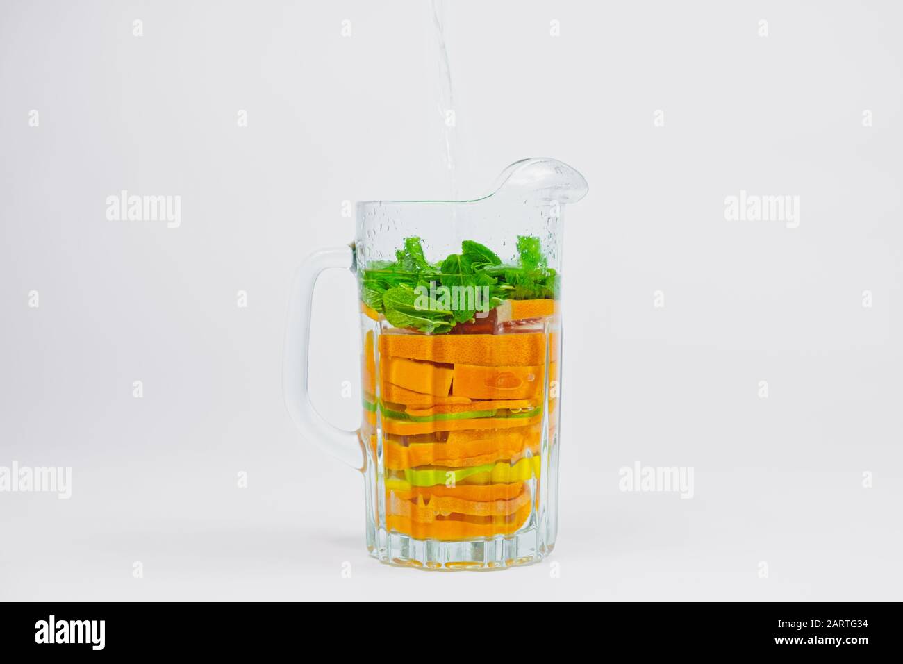 Grande vaso in vetro con agrumi e menta su sfondo bianco. Preparazione della limonata di arance, calce e limoni. Sana e vitamine ricca di frutta dr Foto Stock