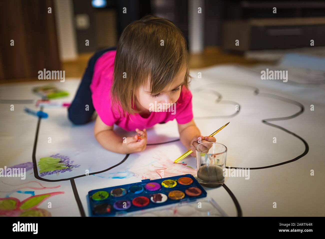 La ragazza di due anni dipinge con i dipinti del manifesto all'interno sul pavimento. Foto Stock