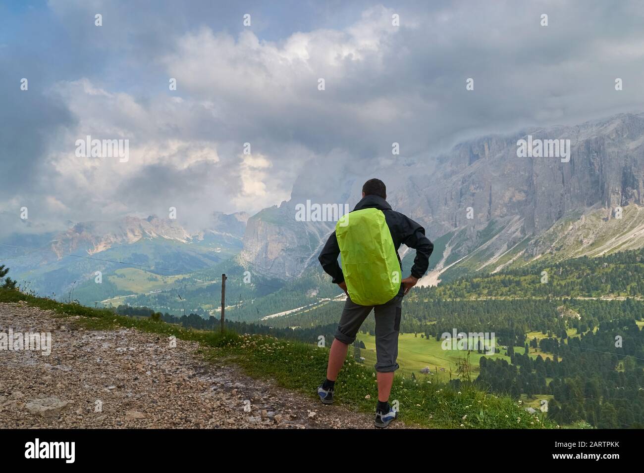 Uomo con zainetto e copertura pioggia verde che guarda le nuvole tempestose verso una valle a monte del Sella nelle Dolomiti, in Italia, durante una h estate Foto Stock