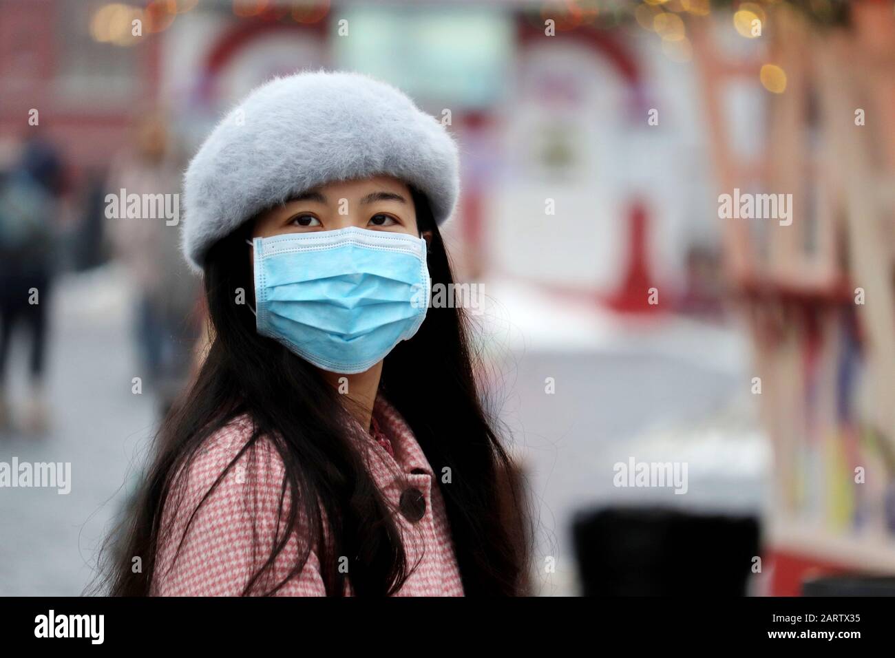 Protezione contro il coronavirus, ragazza cinese in maschera medica protettiva in piedi su una strada invernale della città in folla Foto Stock