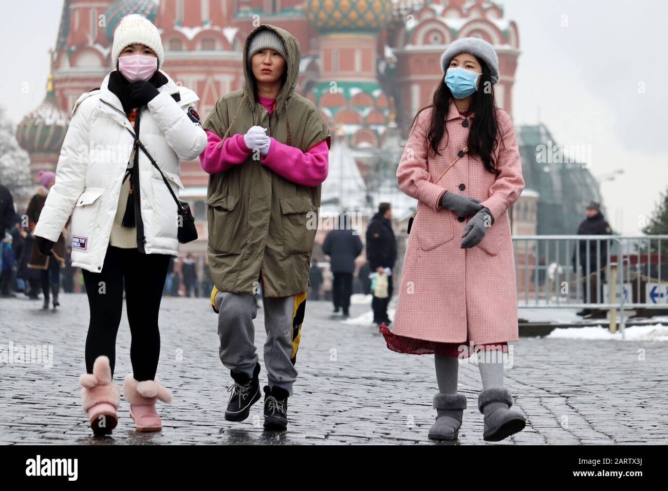 Ragazze cinesi in maschere mediche protettive che camminano su una piazza rossa a Mosca sullo sfondo della Cattedrale dei Santi Basil. Protezione contro il coronavirus Foto Stock