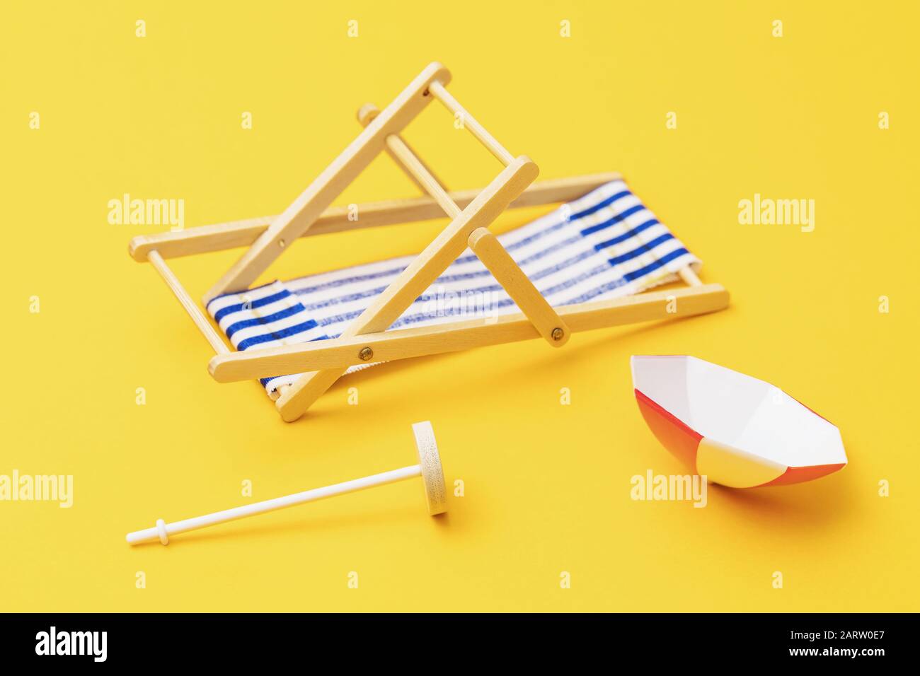 Sedia a sdraio e ombrellone capovolti su sfondo giallo. Concetto di vacanza viziata Foto Stock