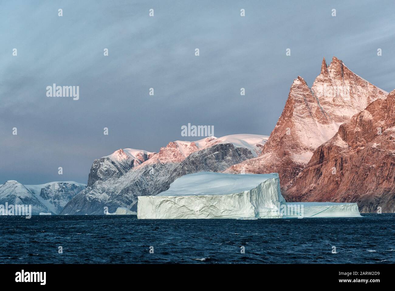 Alba in fiordo Scoresby Sund. Iceberg galleggiante con montagne di colore rossastro. Kangertitivaq, Groenlandia, Danimarca Foto Stock