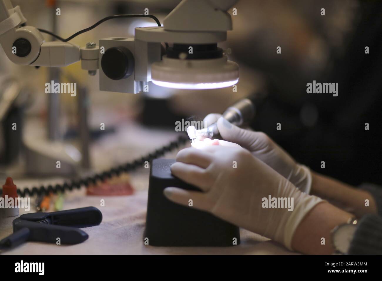 Le mani di un tecnico dentale che elabora una protesi con un trapano al microscopio Foto Stock Le mani di un tecnico dentale che elabora una protesi con un trapano al microscopio Foto Stock