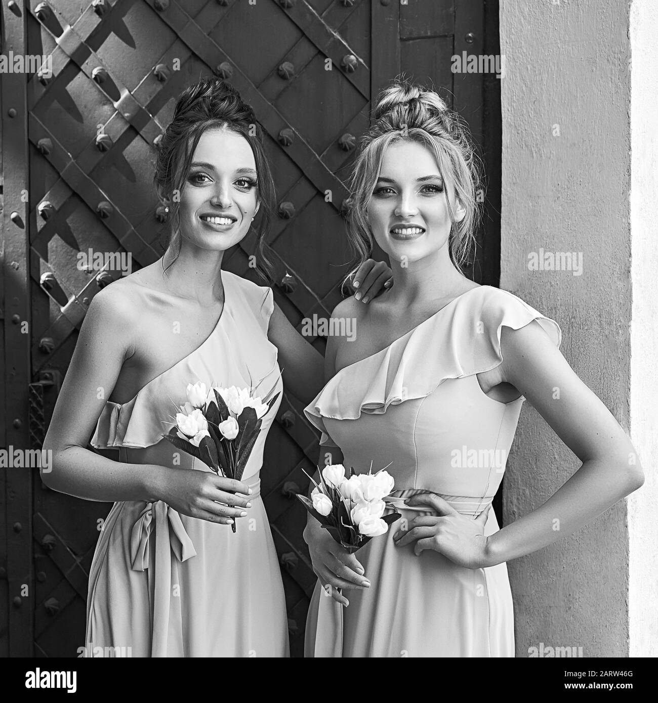 Due belle sposini ragazze bionde e donne brunette indossare elegante full length tulle una spalla abito da sposa e tenere bouquet di fiori Foto Stock