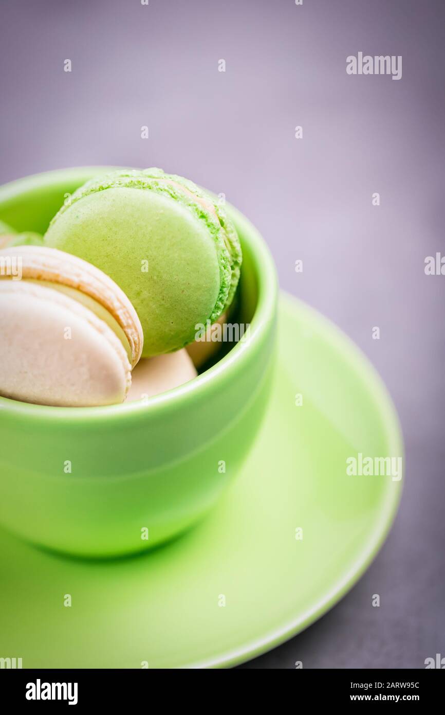 Macaron o macaron francesi fatti in casa. Tazza verde con biscotti. Biscotti alla menta con crema alla vaniglia su sfondo grigio, spazio di copia Foto Stock