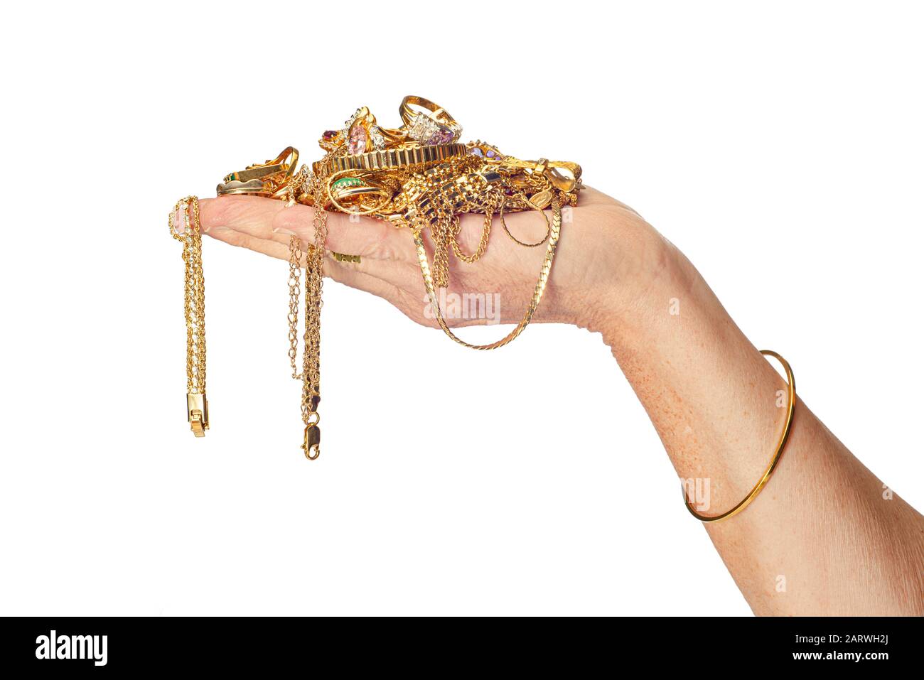 Colpo orizzontale della mano di una donna che tiene un mucchio di gioielli d’oro alcuni dei quali sono appesi dalla sua mano. Indossa anche un braccialetto. Isolato Foto Stock