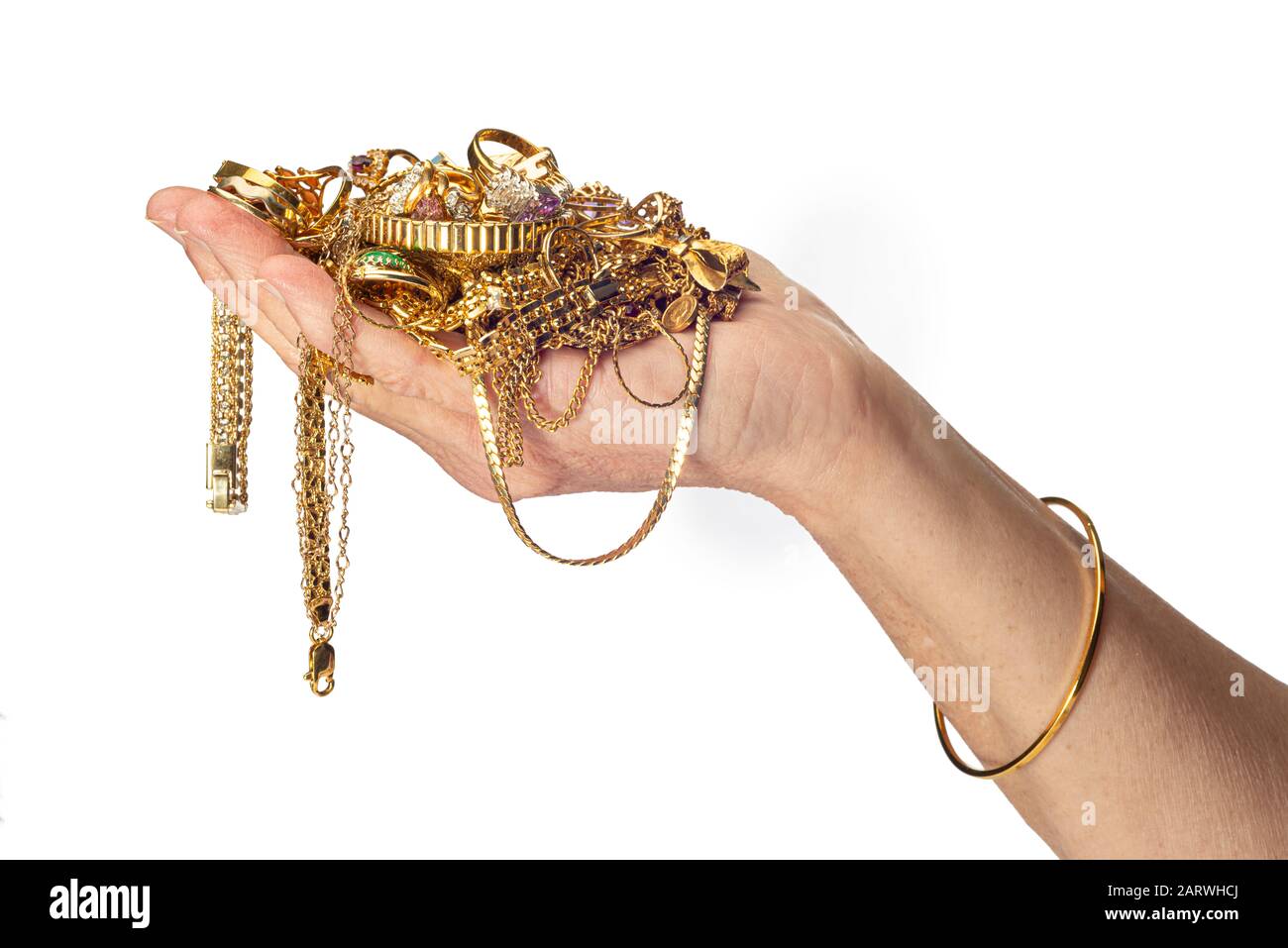 Colpo orizzontale della mano e del braccio di una donna che tiene un mucchio di gioielli in costume d’oro e indossa un braccialetto. Sfondo bianco con spazio di copia. Foto Stock